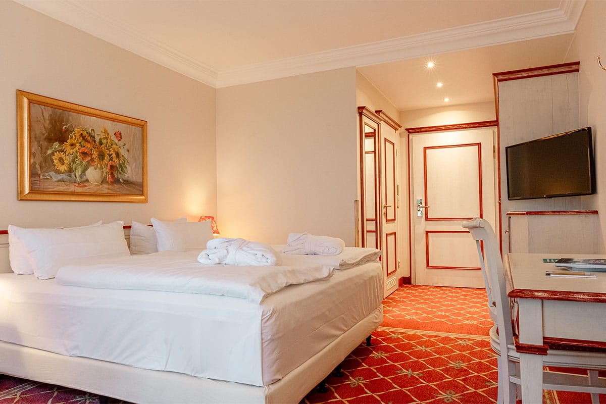 Doppelzimmer mit großem Bett, Schreibtisch, Wandbild und warmen Farben im Rugard Thermal Strandhotel