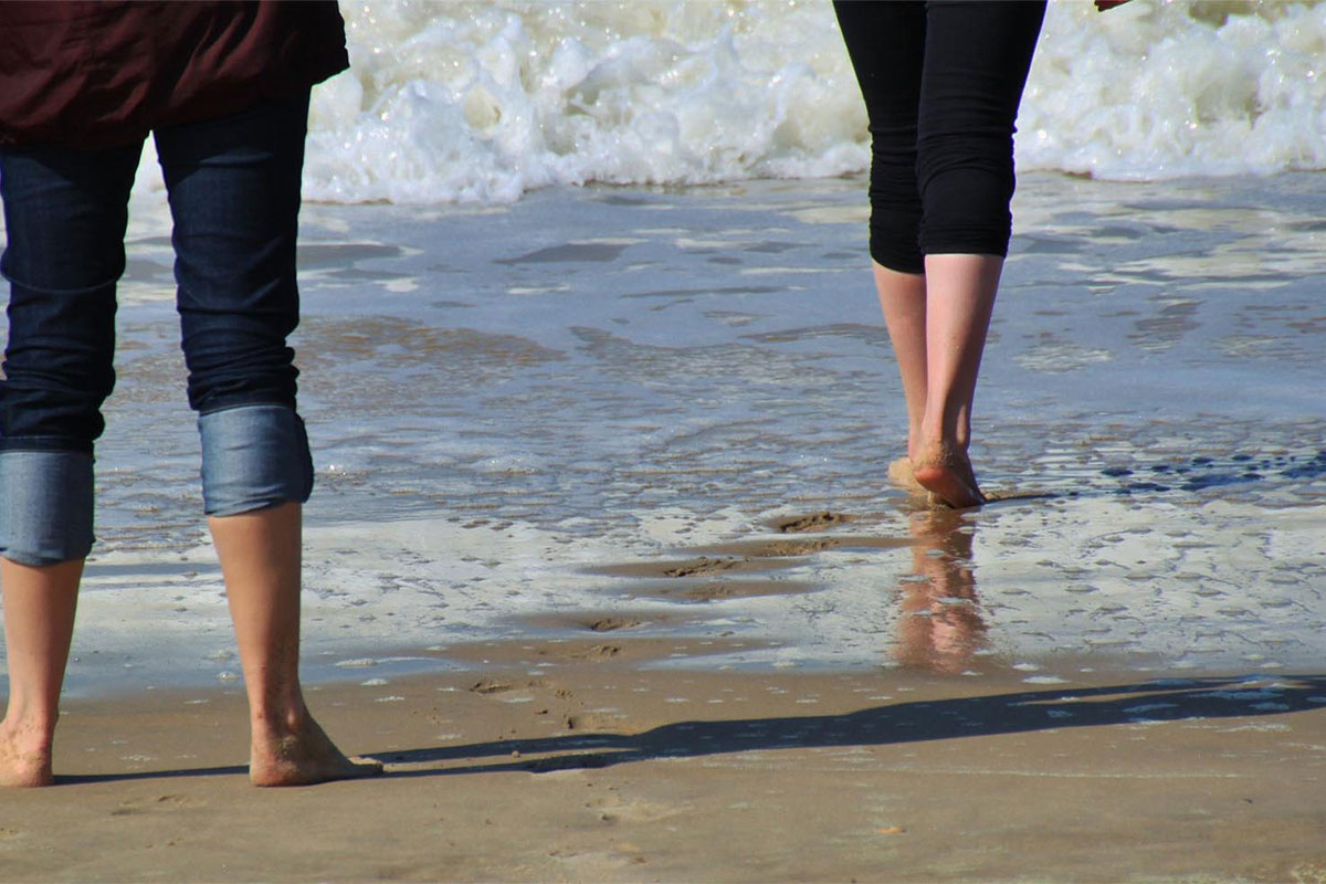 Zwei Personen laufen mit hochgekrempelten Hosen und barfuß ins Meer beim Kneippen im Urlaub im Rugard Thermal Strandhotel.