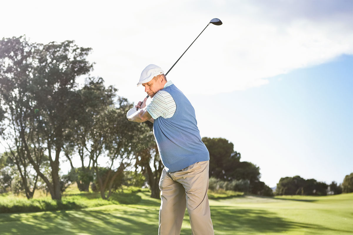 Ein Golfspieler schlägt einen Ball ab, im Hintergrund ein sonniger Golfplatz.