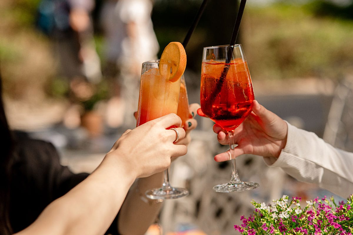 Three people, with only their hands visible, are toasting with cocktails.