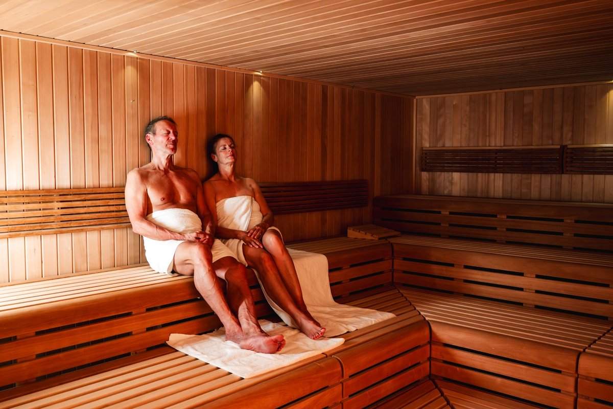 Two women enjoy the warmth of the Finnish sauna on wooden loungers during a wellness session at the Rugard Thermal Strandhotel.