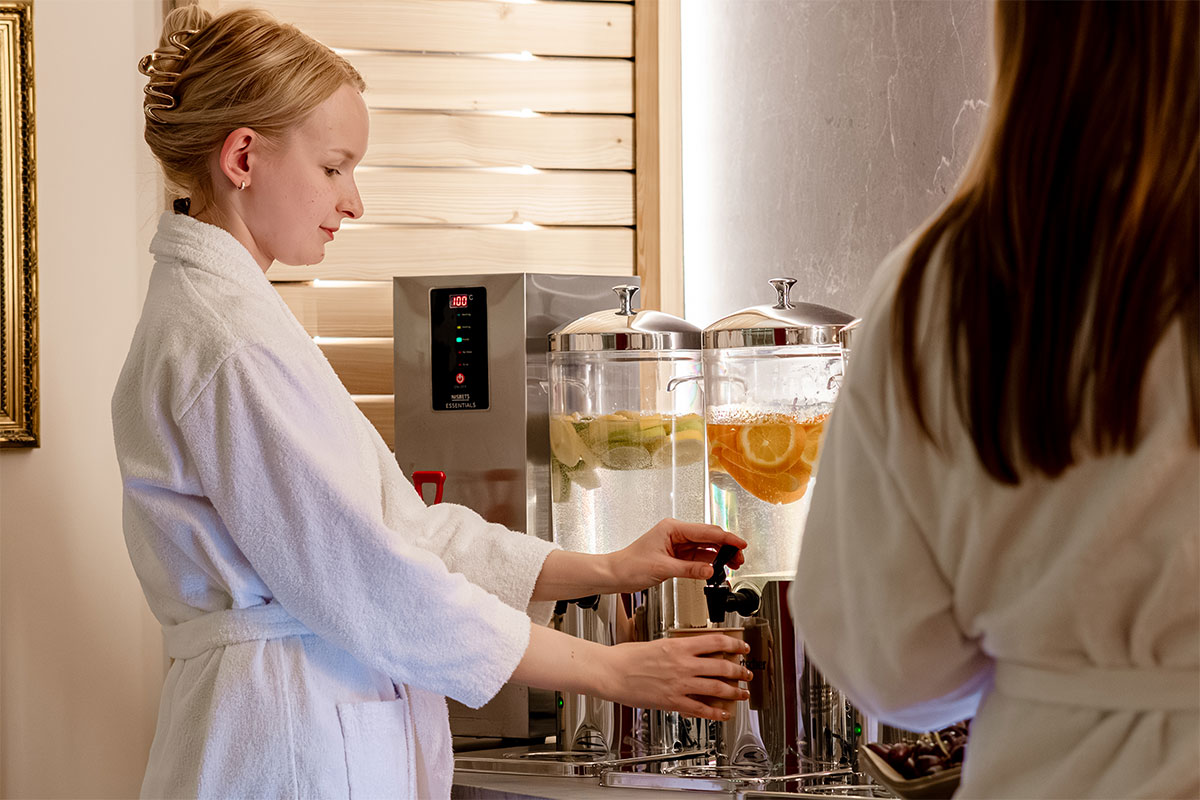 Frau im Bademantel zapft frisches Rügenwasser mit Zitrusfrüchten an der Spa-Bar des Rugard Thermal Strandhotels.
