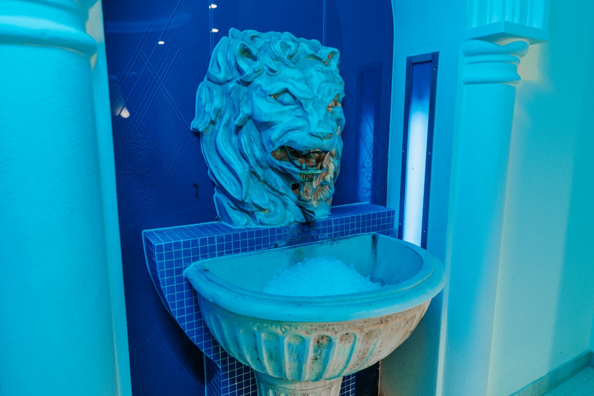 Löwenkopf mit Eisbrunnen unter blauer Beleuchtung, Teil des Wellnessbereichs im Rugard Thermal Strandhotel.