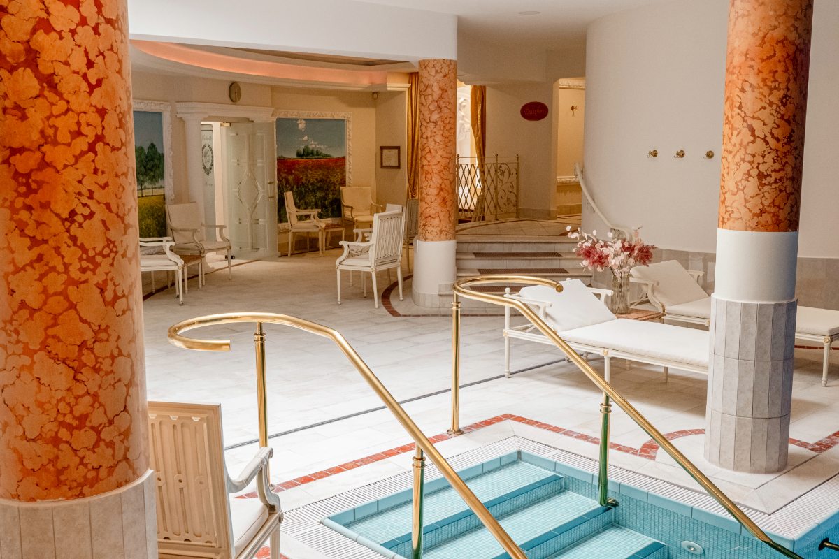 Blick auf Innenpool mit Liegen, Blumenarrangements und warmem Licht im Ruhebereich des Rugard Thermal Hotels.